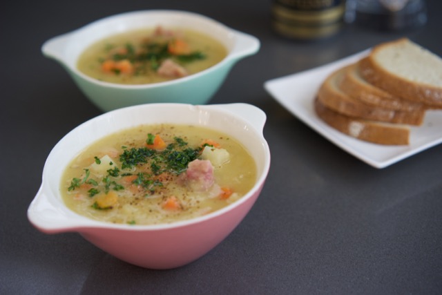 Pink and green bowls with soup topped with parsley, rye bread served on the side