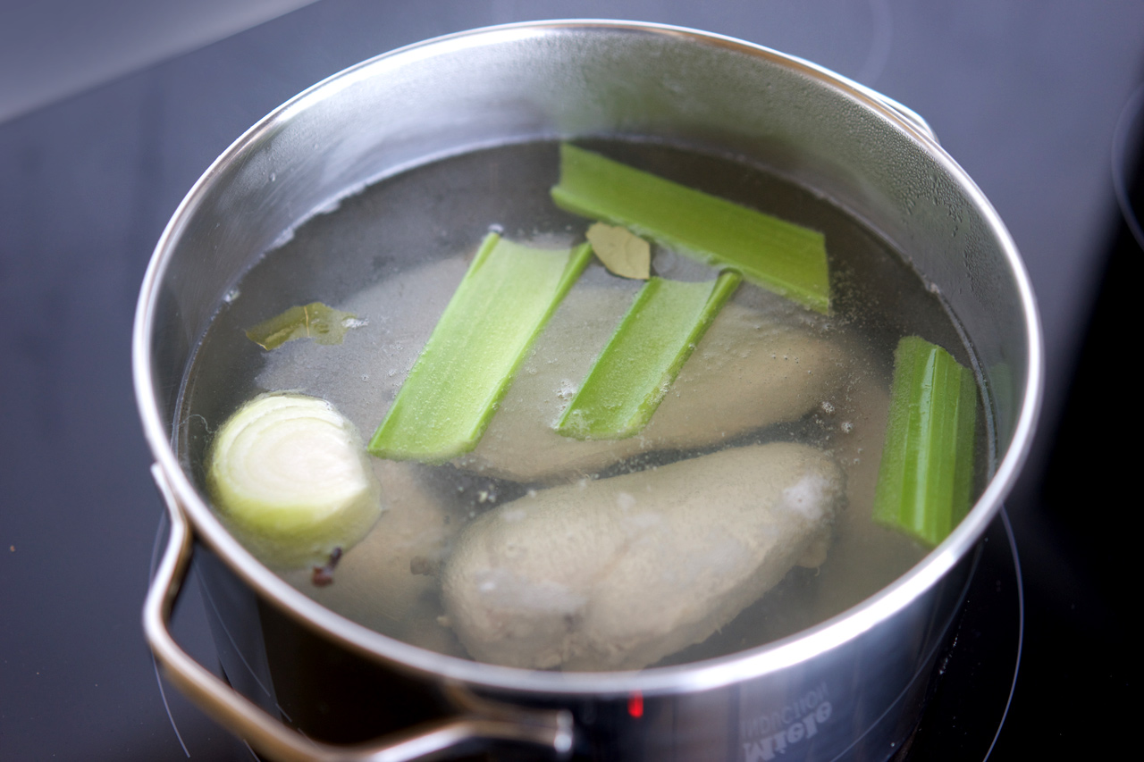 Chicken being poached in water with celery, clove, onion and bay leaf