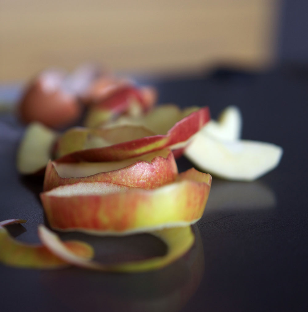 A twirl of apple peels in the foreground with slices in behind. 