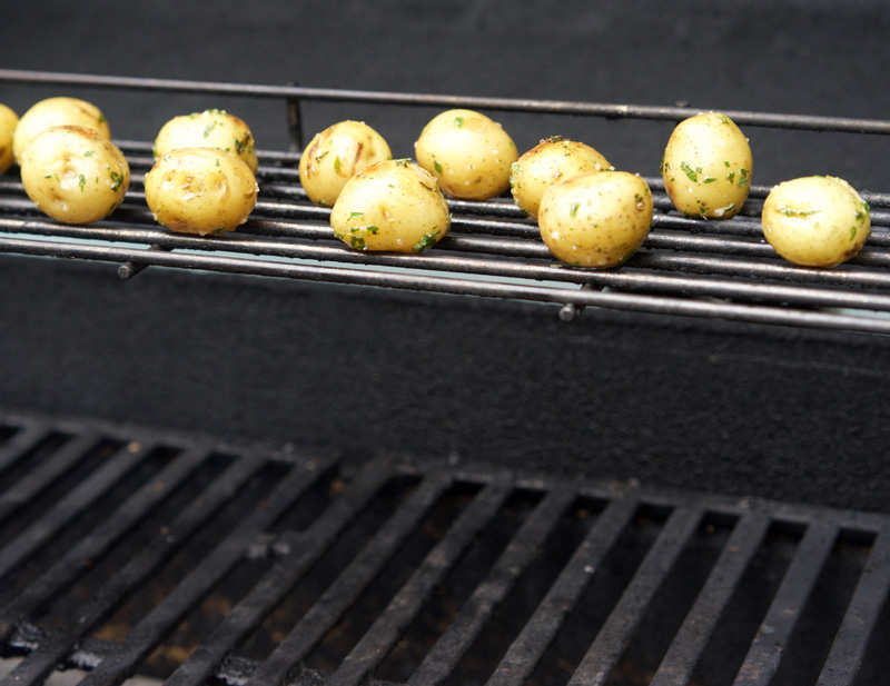 Seasoned baby potatoes roast on the upper rack of the BBQ grill.