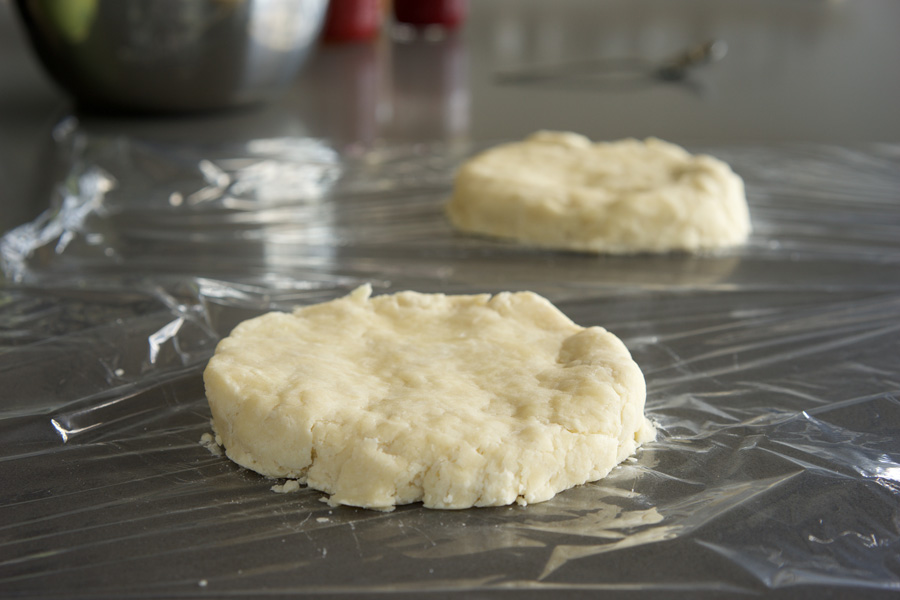 Dough is flattened and placed onto plastic wrap.