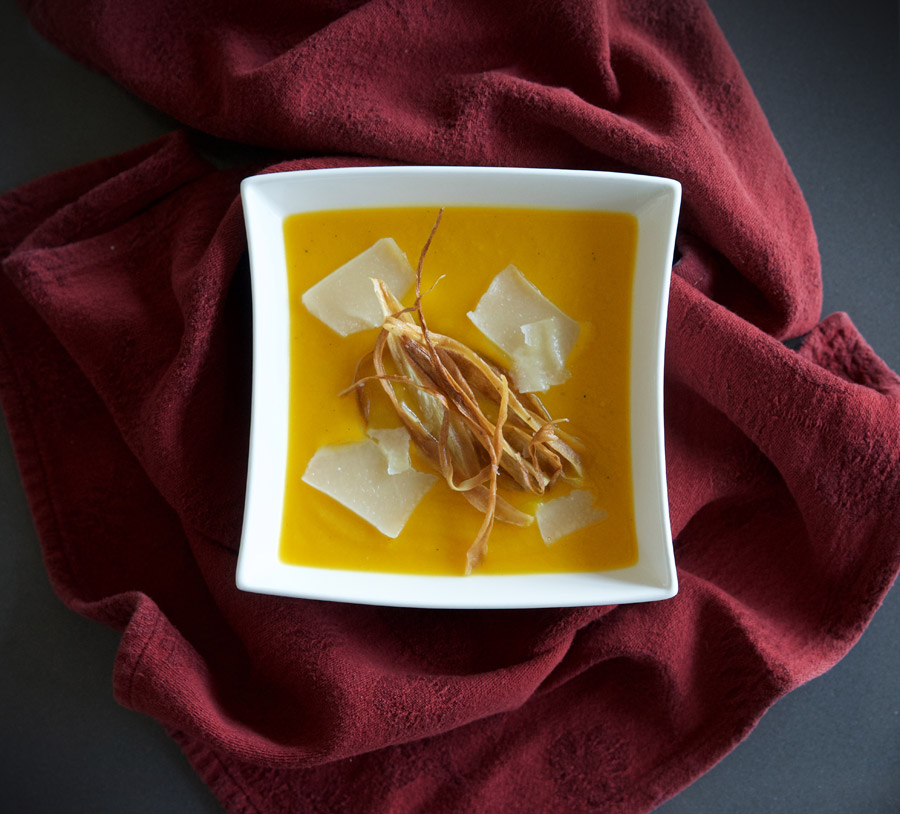Plated butternut soup with parsnip chip garnish on a deep red cloth