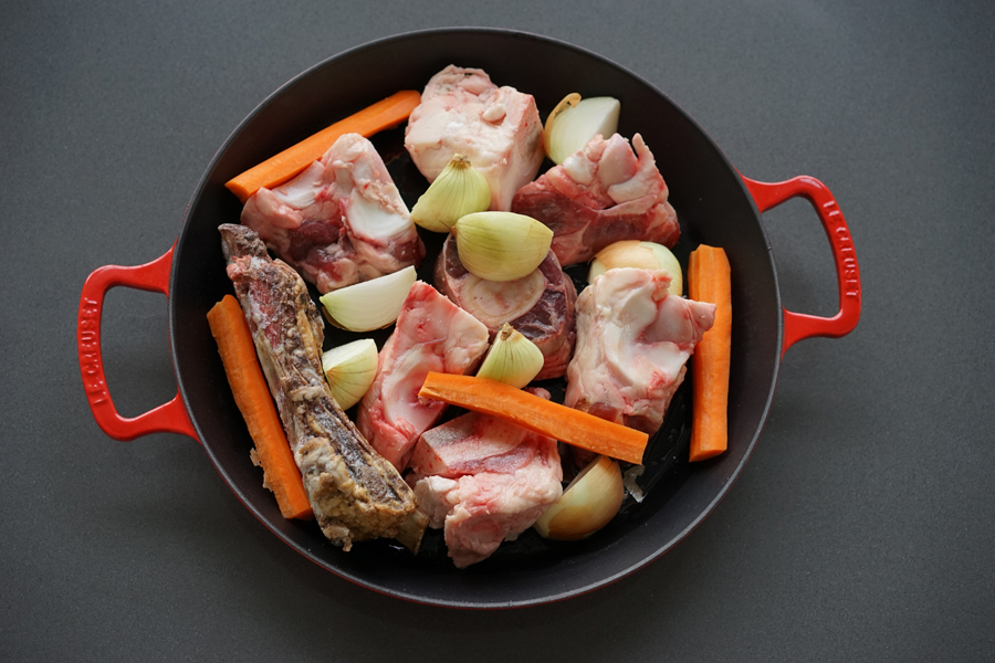 Beef bones in a roasting pan with a few veggies